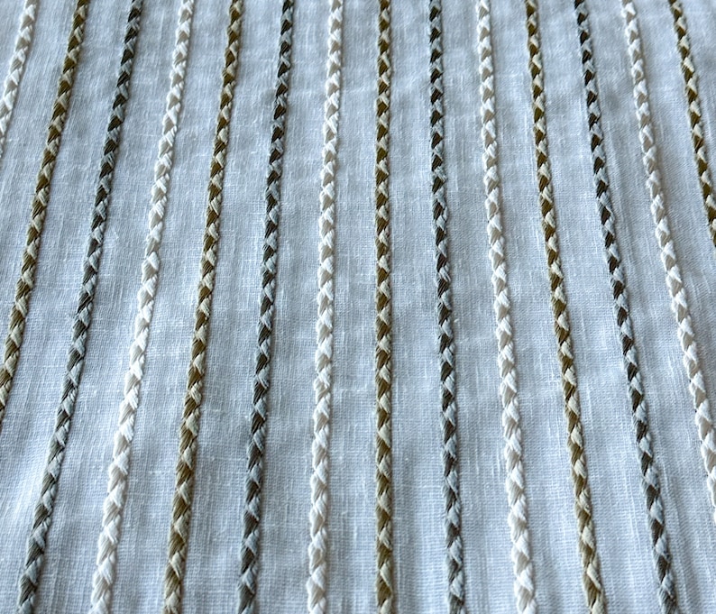 May include: White fabric with vertical stripes of white, gray, and brown thread. The stripes are woven into the fabric and have a textured appearance.