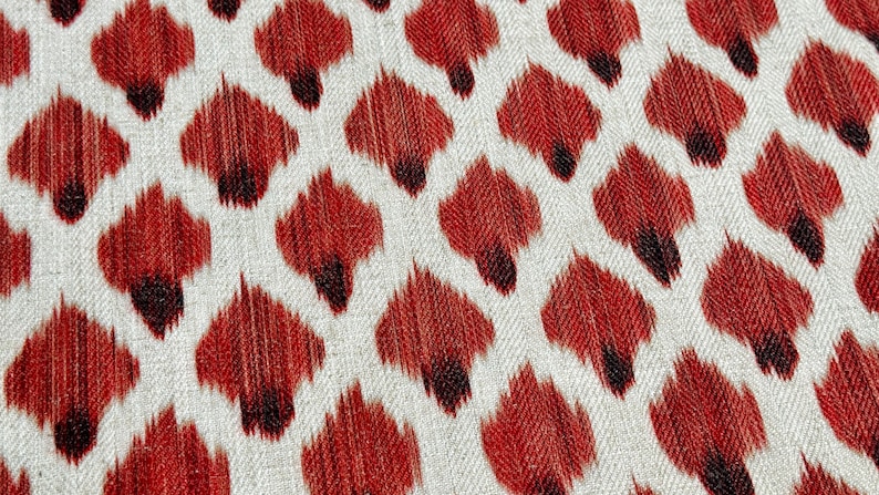 May include: A close-up of a fabric with a repeating pattern of red and black teardrop shapes on a white background.