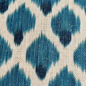 May include: A close-up of a fabric with a blue and white ikat pattern. The fabric has a textured surface and a subtle sheen.