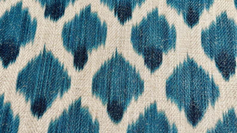 May include: A close-up of a fabric with a blue and white ikat pattern. The fabric has a textured surface and a subtle sheen.