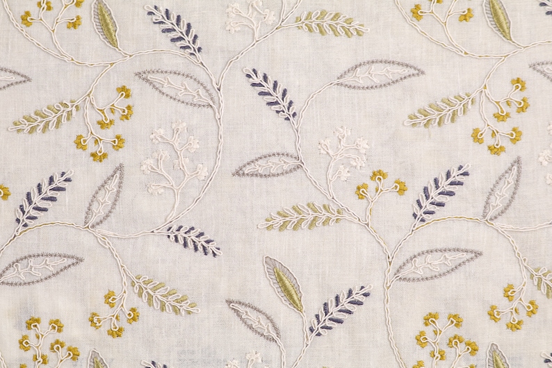 May include: White fabric with an embroidered floral pattern in shades of gray, green, and yellow. The design features delicate leaves and small flower clusters.