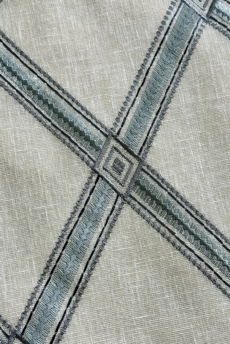 K&ouml;nnte beinhalten: Nahaufnahme eines hellgrauen Stoffes mit einem Kreuzmuster aus blauem und grauem Stickband.