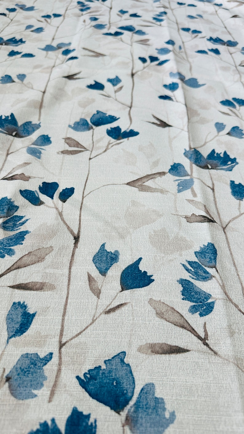 Pu&ograve; includere: Un tessuto bianco con un motivo floreale blu. I fiori sono stilizzati e hanno un effetto acquerello.
