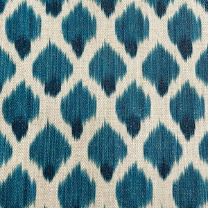 May include: A close-up of a fabric with a repeating pattern of blue and white ikat-style shapes. The fabric has a textured, woven look.