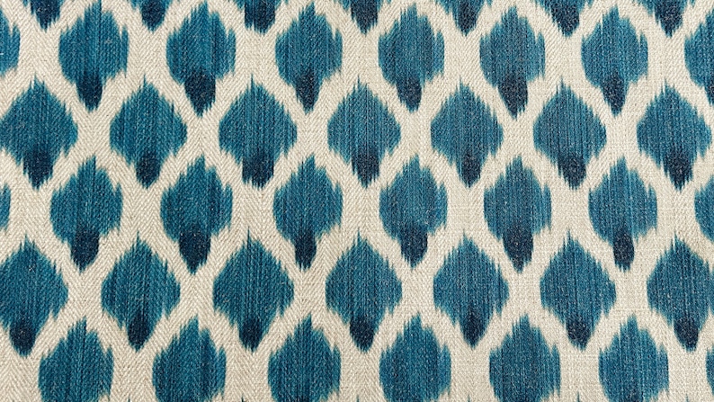 May include: A close-up of a fabric with a repeating pattern of blue and white ikat-style shapes. The fabric has a textured, woven look.