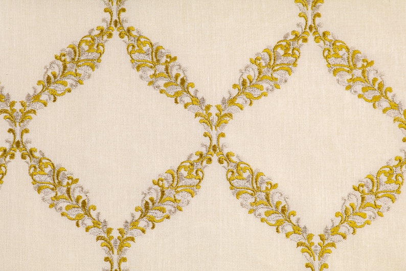 May include: A white fabric with a repeating pattern of gold and silver embroidered diamond shapes. The diamond shapes are made up of a series of stylized floral motifs.