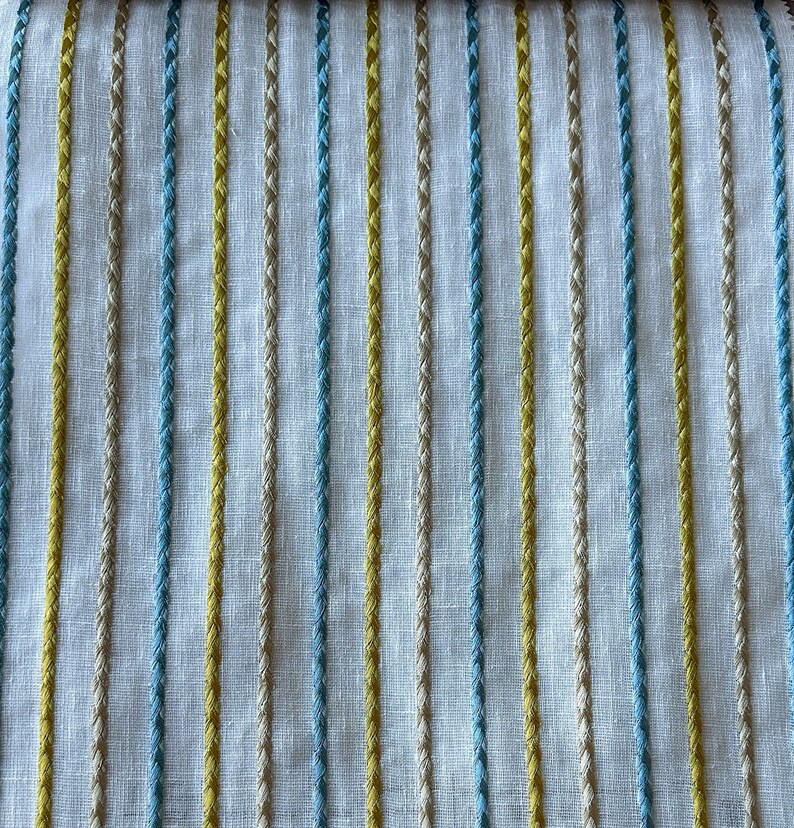 May include: White fabric with vertical stripes of yellow, blue, and beige thread.