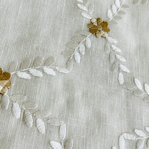 May include: White fabric with embroidered floral design. The flowers are beige and brown with white leaves.