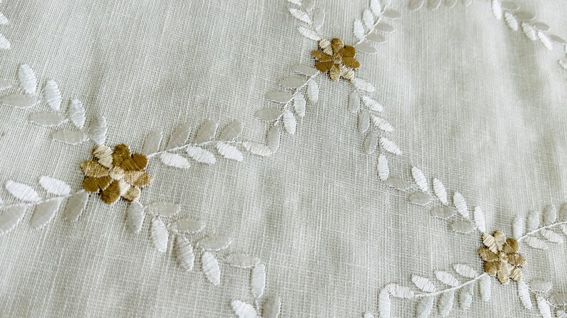May include: White fabric with embroidered floral design. The flowers are beige and brown with white leaves.