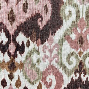 May include: Textile with an ikat pattern in shades of brown, pink, green, and white. The design features stylized floral and geometric shapes, creating a textured, woven appearance. The fabric has a vintage or bohemian aesthetic.