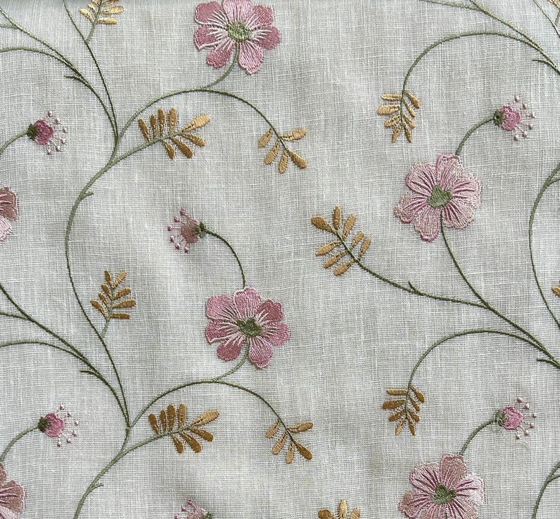 Puede incluir: Una tela blanca con flores rosas y hojas verdes bordadas. La tela tiene una textura de lino sutil.
