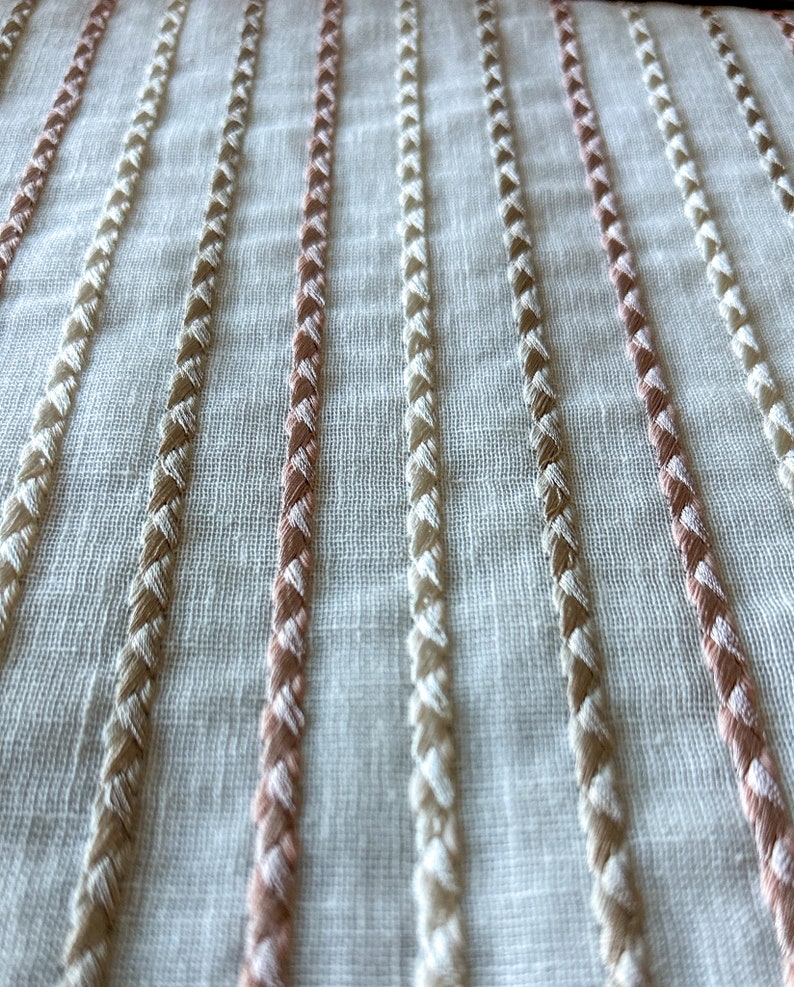 Puede incluir: Tela blanca con filas verticales de costuras bordadas en beige y rosa.