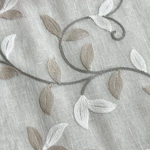 May include: Beige linen fabric with embroidered floral design featuring delicate white and brown leaves.