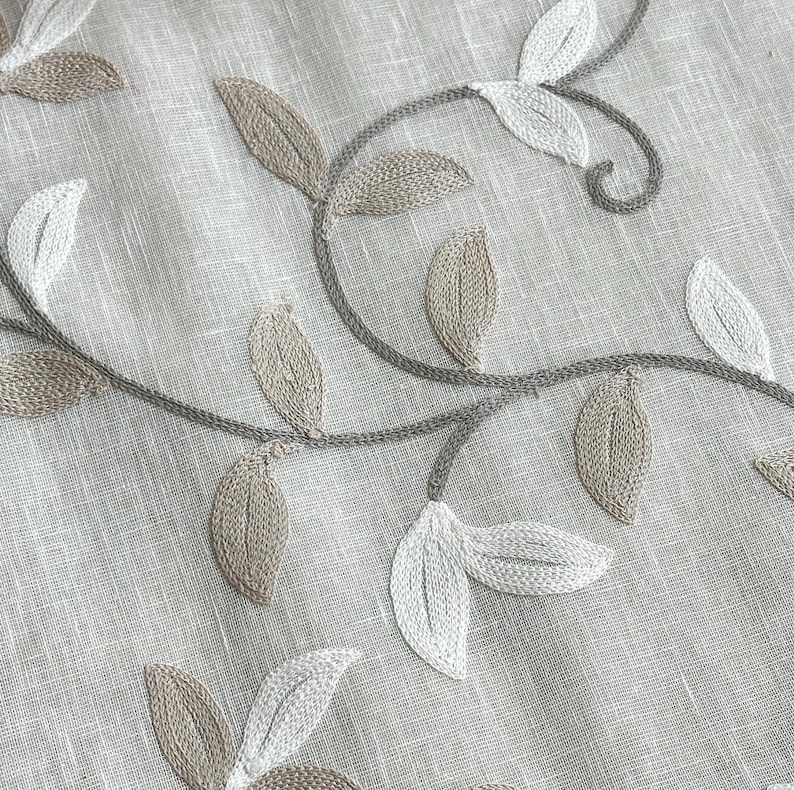 May include: Beige linen fabric with embroidered floral design featuring delicate white and brown leaves.