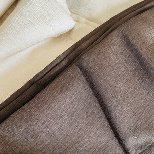 May include: Close-up of folded fabric in shades of brown and off-white. The brown fabric has a textured appearance, while the off-white fabric appears smooth. The image highlights the different textures and colors of the textiles.