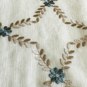 Puede incluir: Primer plano de una tela blanca con un patr&oacute;n floral bordado en marr&oacute;n y azul. El patr&oacute;n presenta peque&ntilde;as flores y hojas.