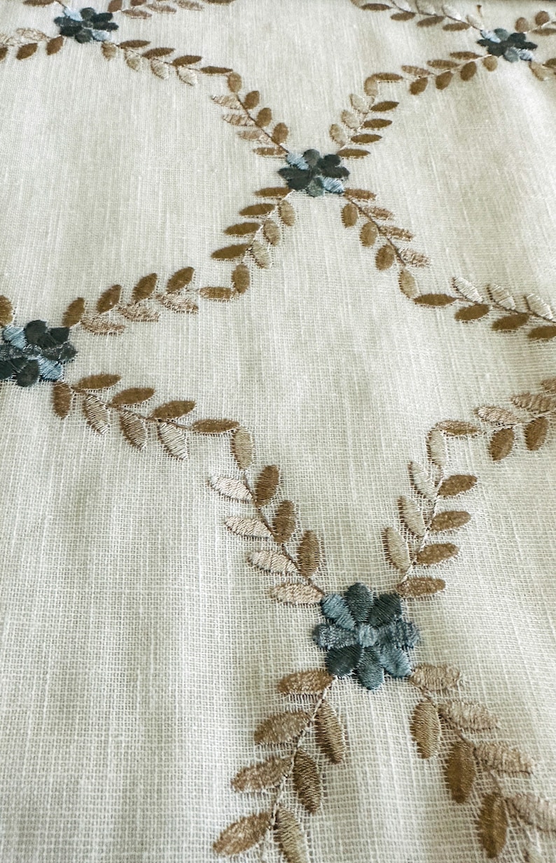 Puede incluir: Primer plano de una tela blanca con un patr&oacute;n floral bordado en marr&oacute;n y azul. El patr&oacute;n presenta peque&ntilde;as flores y hojas.
