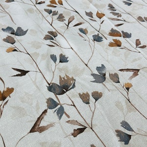 May include: A white fabric with a repeating pattern of brown and blue stylized floral branches. The fabric has a subtle texture.