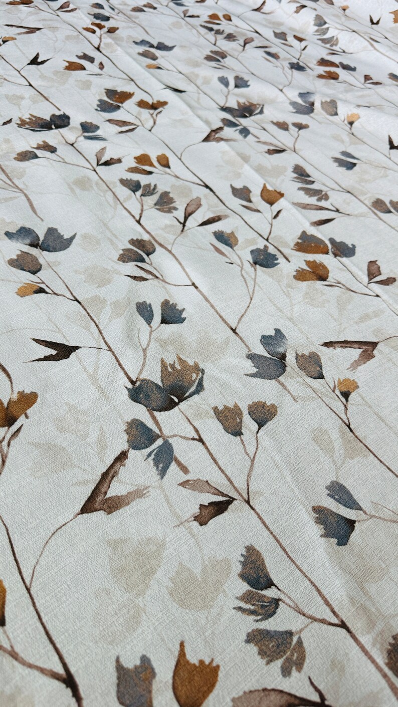 May include: A white fabric with a repeating pattern of brown and blue stylized floral branches. The fabric has a subtle texture.