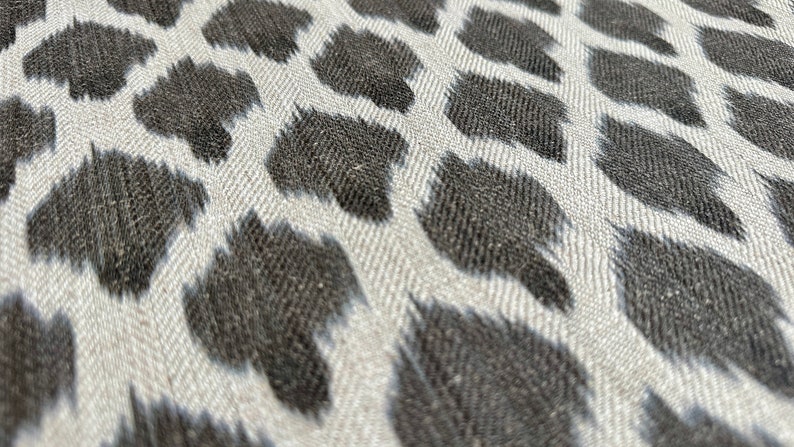 May include: Close-up of a white fabric with a black and white animal print pattern. The fabric has a textured woven look.