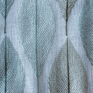 K&ouml;nnte beinhalten: Ein wei&szlig;er Stoff mit einem sich wiederholenden Muster aus hellblauen und grauen Bl&auml;ttern. Die Bl&auml;tter sind mit einem zarten, strukturierten Design bestickt.