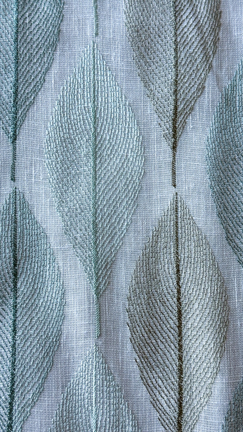 K&ouml;nnte beinhalten: Ein wei&szlig;er Stoff mit einem sich wiederholenden Muster aus hellblauen und grauen Bl&auml;ttern. Die Bl&auml;tter sind mit einem zarten, strukturierten Design bestickt.