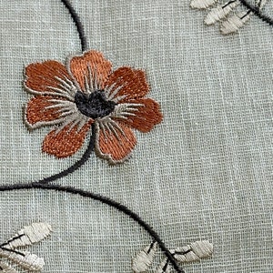K&ouml;nnte beinhalten: Nahaufnahme eines wei&szlig;en Stoffes mit braunen und grauen gestickten Blumen und Bl&auml;ttern.