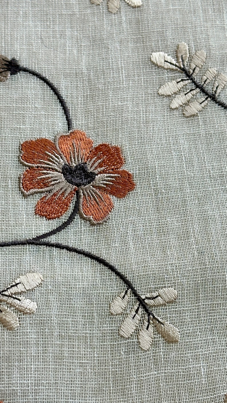 K&ouml;nnte beinhalten: Nahaufnahme eines wei&szlig;en Stoffes mit braunen und grauen gestickten Blumen und Bl&auml;ttern.