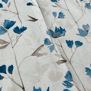 Pu&ograve; includere: Primo piano di un tessuto bianco con un motivo floreale blu. Il tessuto ha una texture sottile e i fiori sono dipinti in stile acquerello.