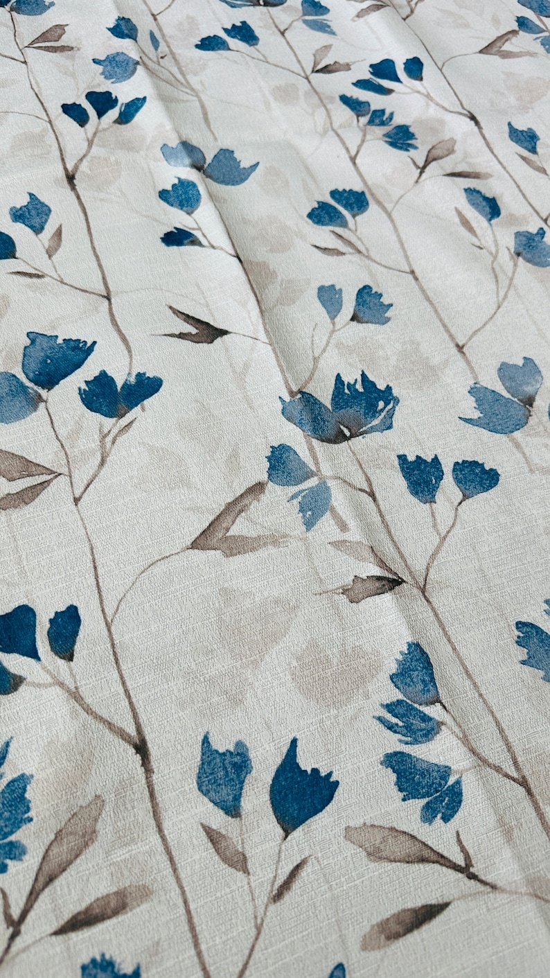 Pu&ograve; includere: Primo piano di un tessuto bianco con un motivo floreale blu. Il tessuto ha una texture sottile e i fiori sono dipinti in stile acquerello.