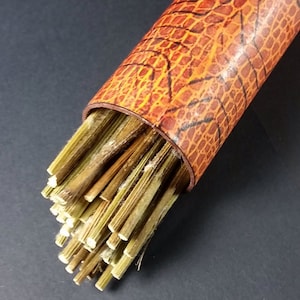 May include: A bundle of dried, light brown, natural plant stems in a tube with a brown and orange patterned design.