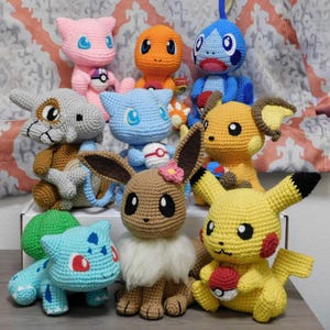 Peut inclure: Collection de peluches Pokémon crochetées à la main, de différentes couleurs. Les peluches incluent Pikachu, Eevee, Bulbasaur, Charmander, Squirtle, et d'autres. Chaque peluche a des détails et est faite de fil doux.
