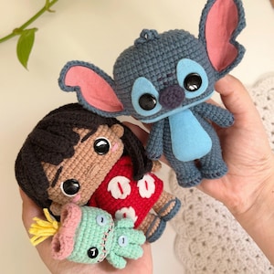 Peut inclure: Figurines crochetées de Lilo, Stitch et d'un petit extraterrestre vert. Lilo porte une robe rouge avec des détails de fleurs blanches. Stitch est bleu avec de grandes oreilles et un ventre bleu. L'alien vert a un nœud rose.