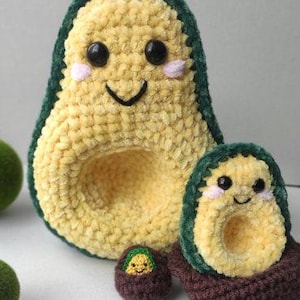 Może przedstawiać: Zestaw trzech szydełkowych awokado. Duże awokado jest żółte z zieloną obwódką, czarnymi oczami, różowymi policzkami i uśmiechniętą twarzą. Mniejsze awokado jest brązowe z zieloną obwódką i uśmiechniętą twarzą. Najmniejsze awokado jest brązowe z żółtym awokado w środku.