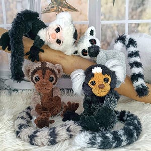 May include: A collection of handmade plush monkey toys in various colors and patterns. The monkeys are positioned on a branch and a fluffy white surface. The plush toys have detailed features, including expressive faces and long, patterned tails.