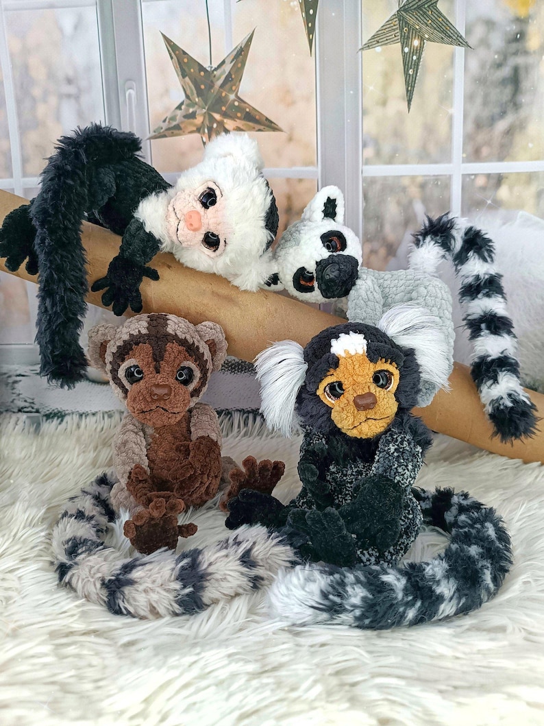 May include: A collection of handmade plush monkey toys in various colors and patterns. The monkeys are positioned on a branch and a fluffy white surface. The plush toys have detailed features, including expressive faces and long, patterned tails.