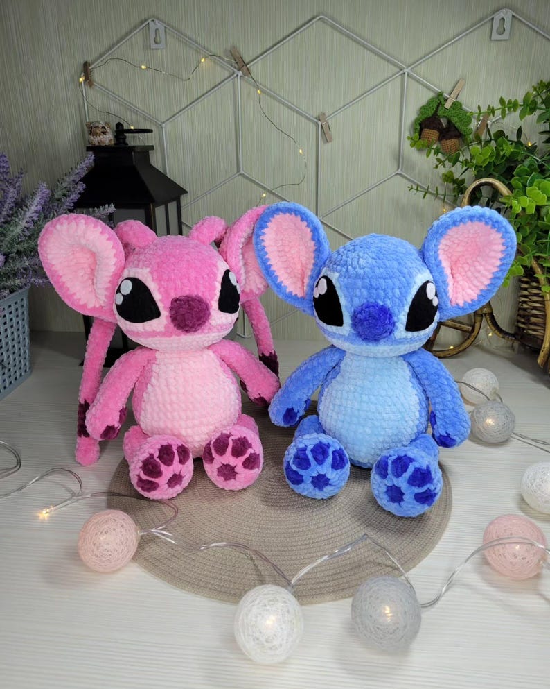 May include: Two plush toys, one pink and one blue, resembling cartoon characters. The pink toy has long ears and a dark pink nose and feet. The blue toy has large ears and a blue nose and feet. Both have large black eyes.