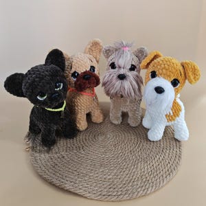 Peut inclure: Quatre figurines de chiens au crochet faits à la main, en noir, beige et blanc, avec des détails tels que des oreilles tombantes et des yeux expressifs. Ils sont disposés sur un tapis rond en jute tressé, créant une charmante présentation.