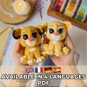 May include: Two small, handcrafted crochet lion cub figures featuring golden-yellow yarn, white muzzles, and large black safety eyes. One cub has dark brown ear tips. Both figures are seated with detailed paw stitching and pink embroidered noses.