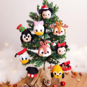 Peut inclure: Un petit sapin de Noël orné de décorations faites à la main au crochet représentant des personnages de dessins animés. Les ornements incluent Mickey Mouse, Minnie Mouse, Donald Duck, Daisy Duck, Chip et Dale et Pluto. L'arbre est sur une base en bois.