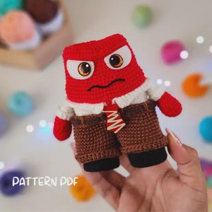 May include: A crocheted plush toy of the character Anger from the movie Inside Out. The toy is red with a white shirt, brown trousers, and a red and white tie. The toy has a furrowed brow, angry eyes, and a frown.