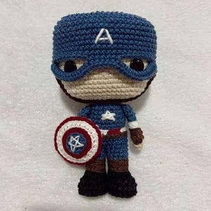 May include: A handmade Captain America amigurumi doll. The doll is crocheted with blue, beige, red, white, brown, and black yarn. It features a blue helmet with a white "A", a shield, and a star on the chest.