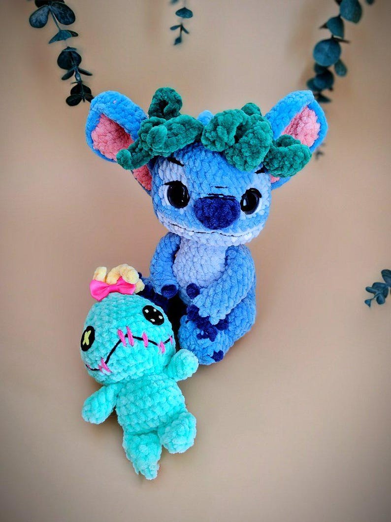 May include: Two handmade crochet plush toys. One is blue with a green headpiece and pink inner ears. The other is turquoise with pink stitching and a yellow bow. Both have black button eyes.