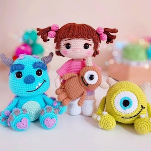 Puede incluir: Muñecos de ganchillo inspirados en la película Monstruos, S.A. Los muñecos incluyen un monstruo azul con cuernos, un monstruo amarillo con un ojo y una muñeca de una niña sosteniendo un monstruo marrón. Los muñecos están hechos a mano con detalles.