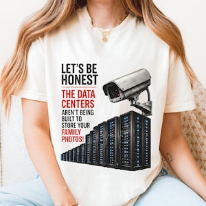 May include: An ivory t-shirt featuring a graphic of a row of black server racks topped with a security camera. The text reads: LET'S BE HONEST THE DATA CENTERS AREN'T BEING BUILT TO STORE YOUR FAMILY PHOTOS! The word IVORY is printed in the top left corner.