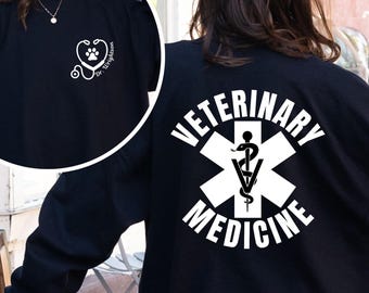 May include: Black sweatshirt with white text and graphics. The front features a stethoscope and paw print design. The back displays "VETERINARY MEDICINE" around a medical symbol. A person is wearing the sweatshirt.