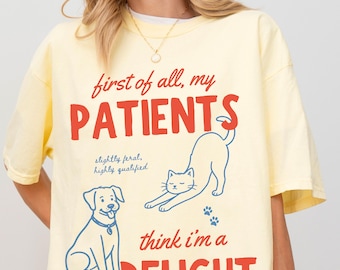 May include: Yellow t-shirt with the text "first of all, my PATIENTS" in red, and "think i'm a DELIGHT" in red. The shirt features a blue dog and cat illustration. The text "slightly feral, highly qualified" is also included.