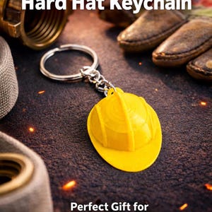May include: A yellow hard hat keyring with a silver chain. The keyring is a miniature replica of a construction worker's hard hat. The image also includes the text "Hard Hat Keychain".