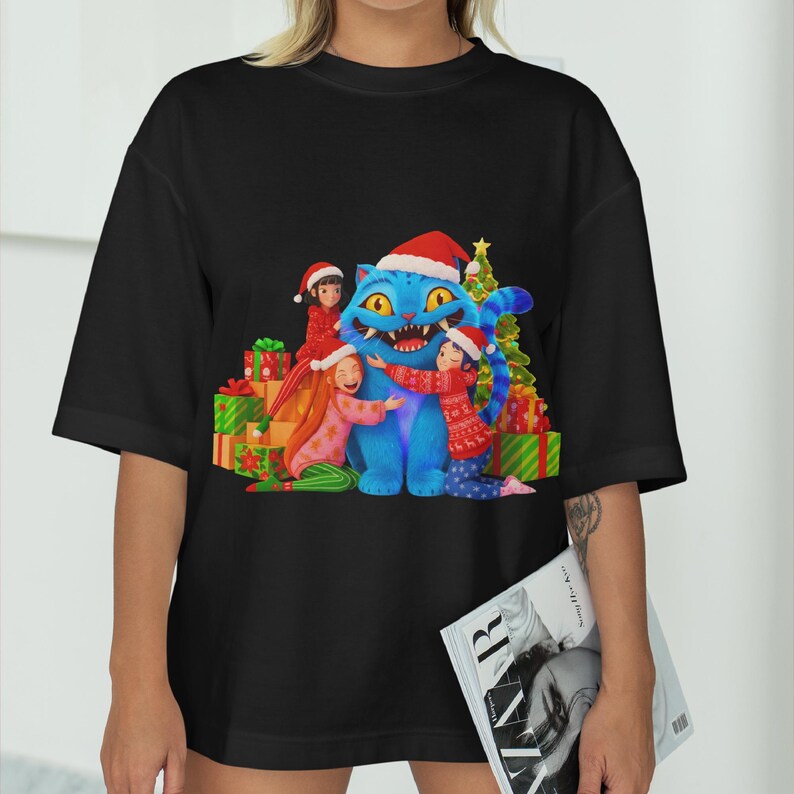 K&ouml;nnte beinhalten: Schwarzes T-Shirt mit einem weihnachtlichen Motiv. Das Design zeigt eine blaue Katze mit Weihnachtsm&uuml;tze, umgeben von Kindern und Geschenken. Ein Weihnachtsbaum ist ebenfalls zu sehen.