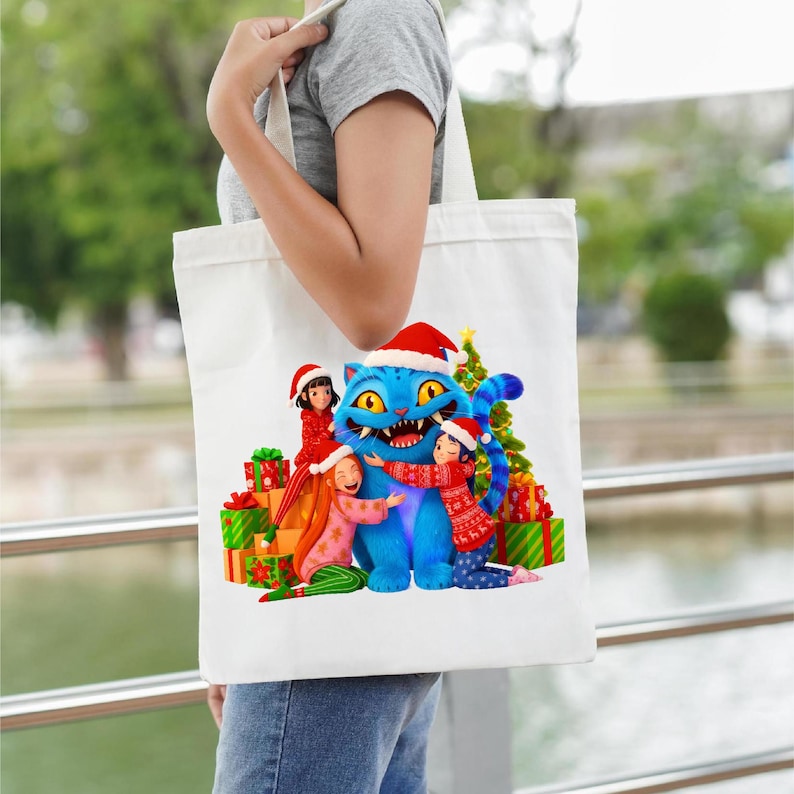 K&ouml;nnte beinhalten: Wei&szlig;e Tragetasche mit einer festlichen Illustration einer blauen Katze mit Weihnachtsm&uuml;tze, die von Kindern mit Weihnachtsm&uuml;tzen und Weihnachtspullovern umarmt wird. Geschenke und ein Weihnachtsbaum vervollst&auml;ndigen das Design.